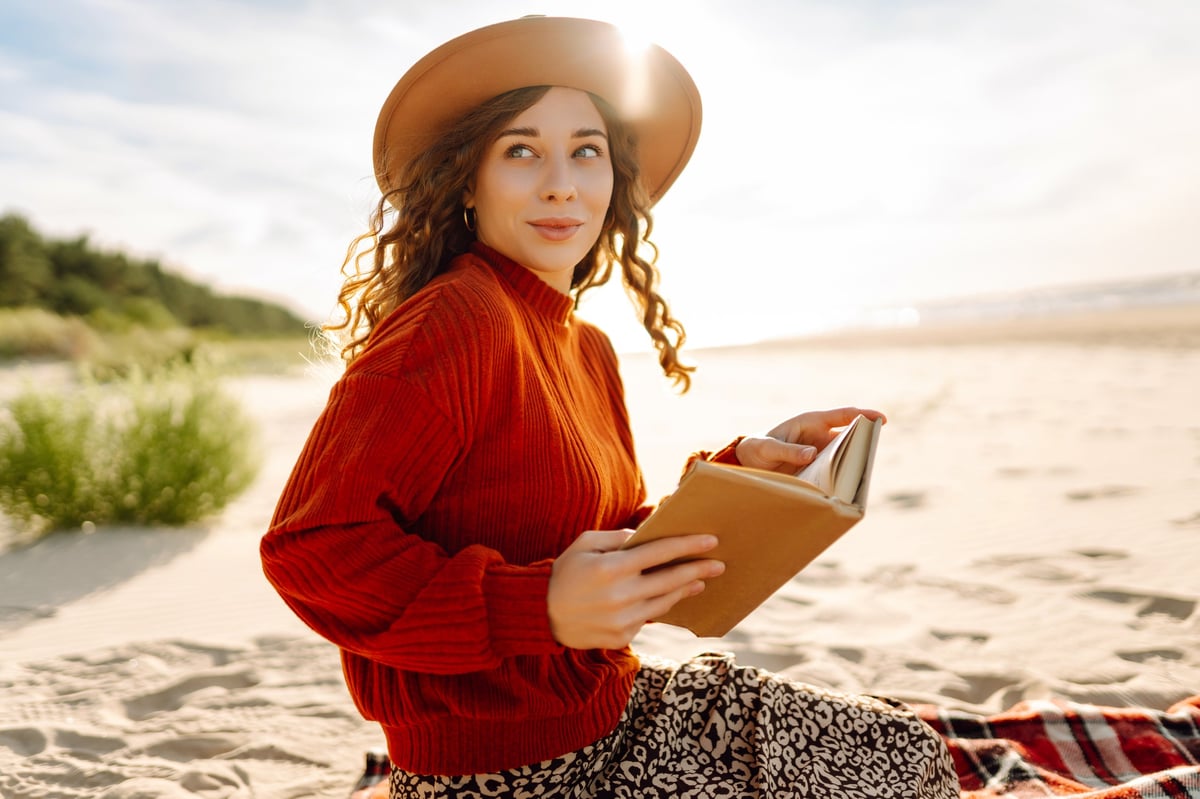 Young woman reading a book by the sea at sunset