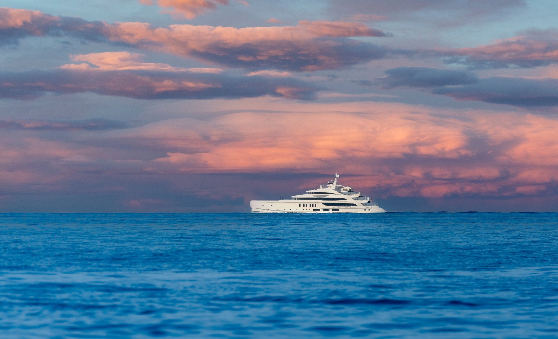 A luxurious yacht sails across the calm ocean under a stunning, colorful sunset sky