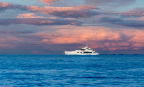 Luxury yacht sailing across calm ocean at sunset