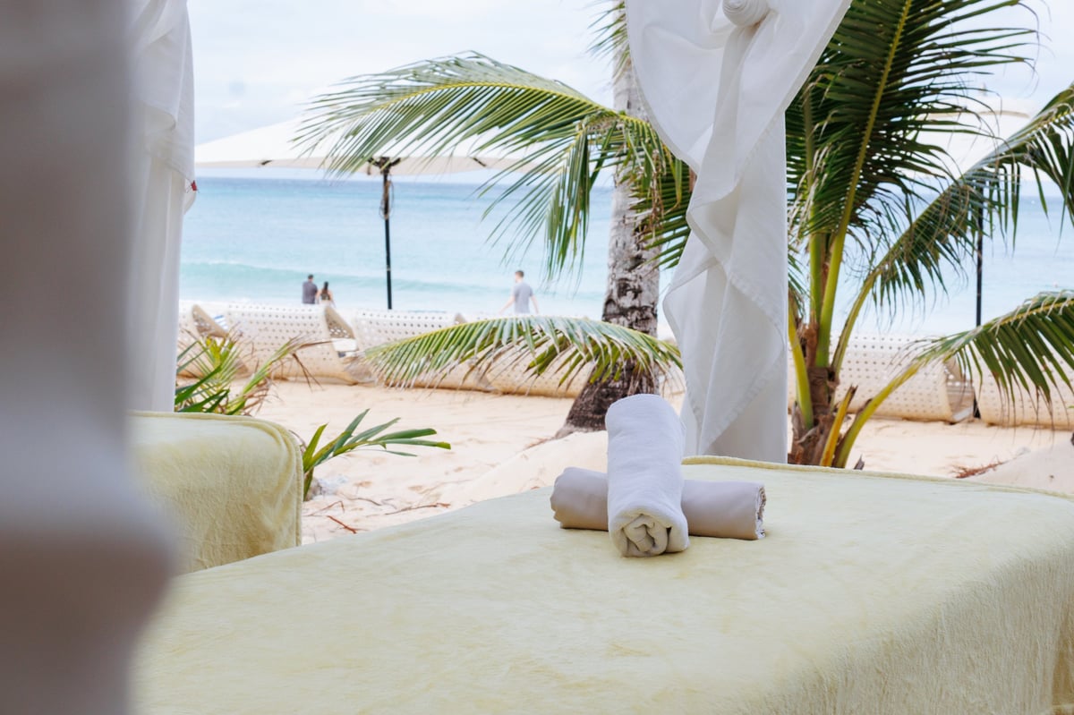 Tranquil beachfront wellness setup with massage tables under a canopy, surrounded by palm trees and the ocean