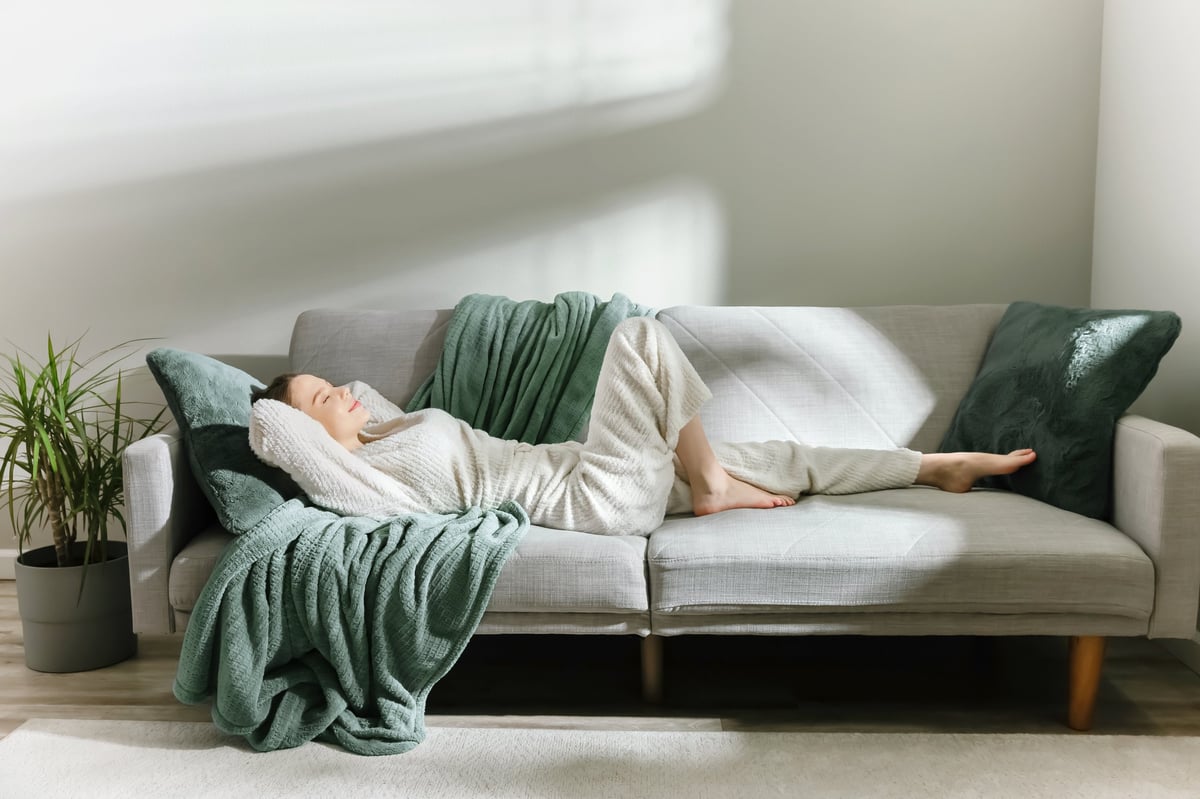Woman in soft loungewear resting on a modern sofa in natural light, a peaceful and calming wellness mood