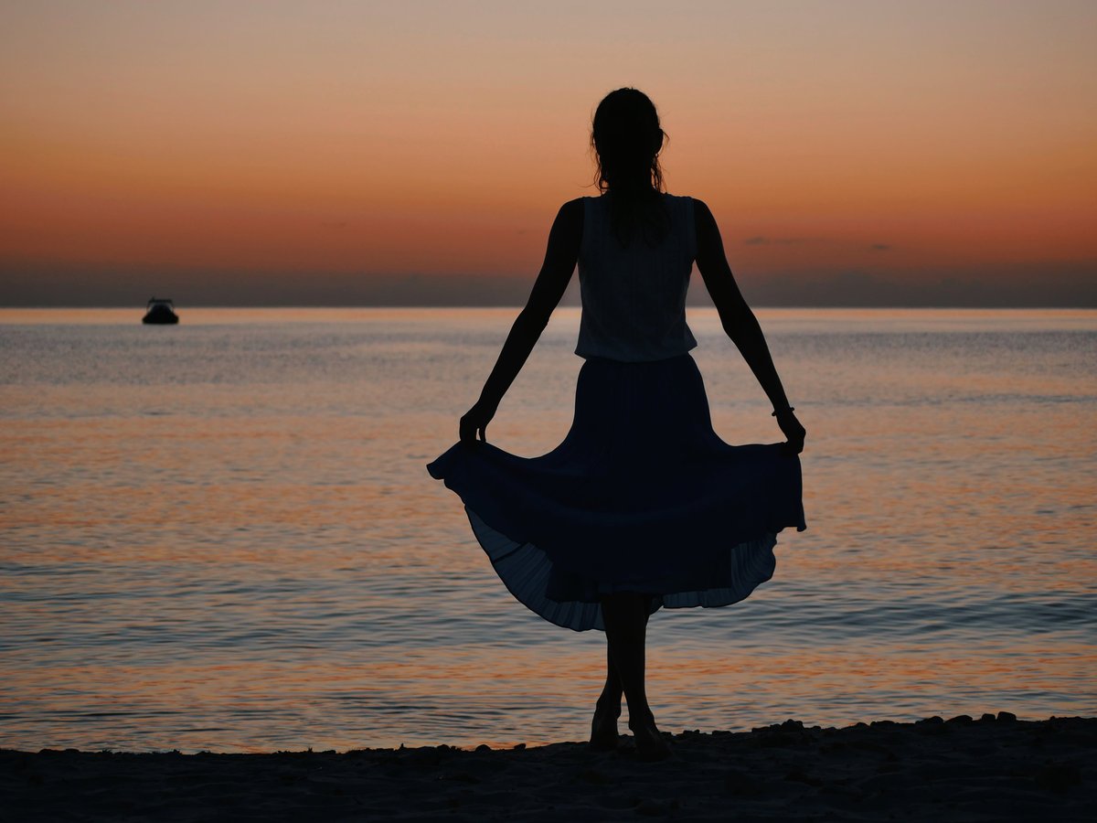 Silhouette of a woman standing on the beach at sunset