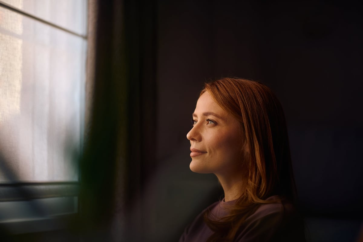 Pensive woman looking through the window while enjoying a day at home