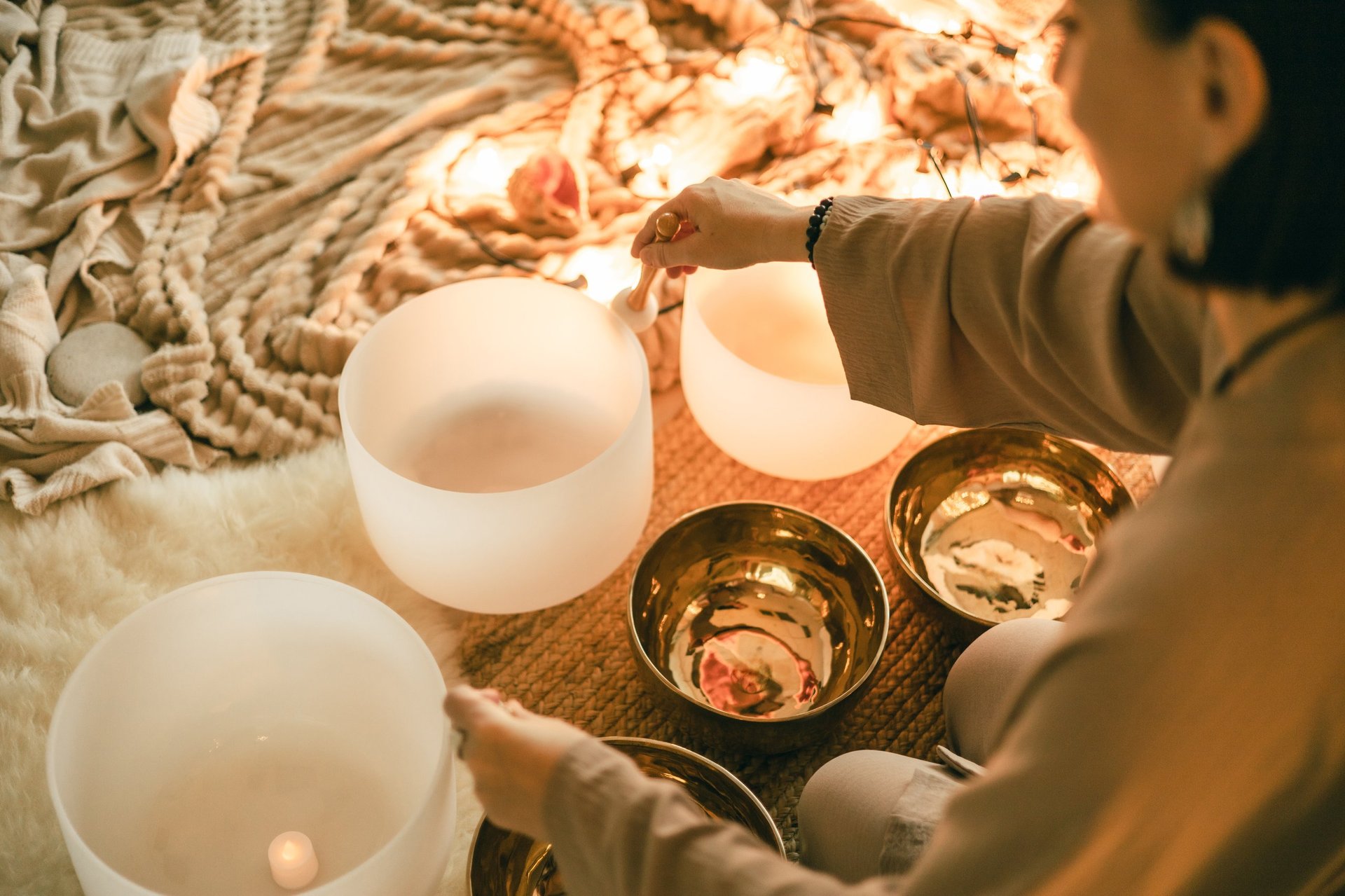 A woman practices sound healing with crystal and metal bowls surrounded by glowing candles, symbolizing feminine energy, mindfulness, and calm during a relaxing meditation retreat.