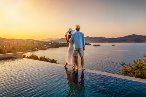 Couple by the swimming pool enjoying a sunset behind the sea