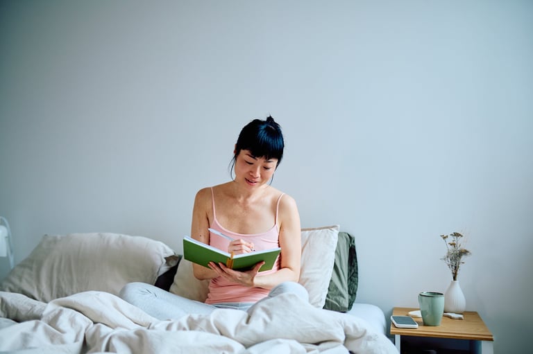 Woman sitting in bed writing in a notebook, practicing mindfulness and self-reflection during her morning routine