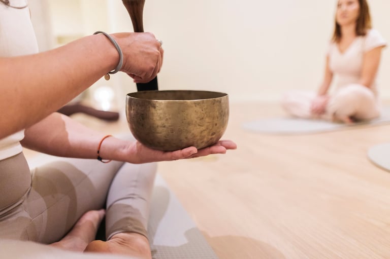 Woman playing a singing bowl during a sound healing session, creating peaceful vibrations for individuals practicing mindfulness and relaxation