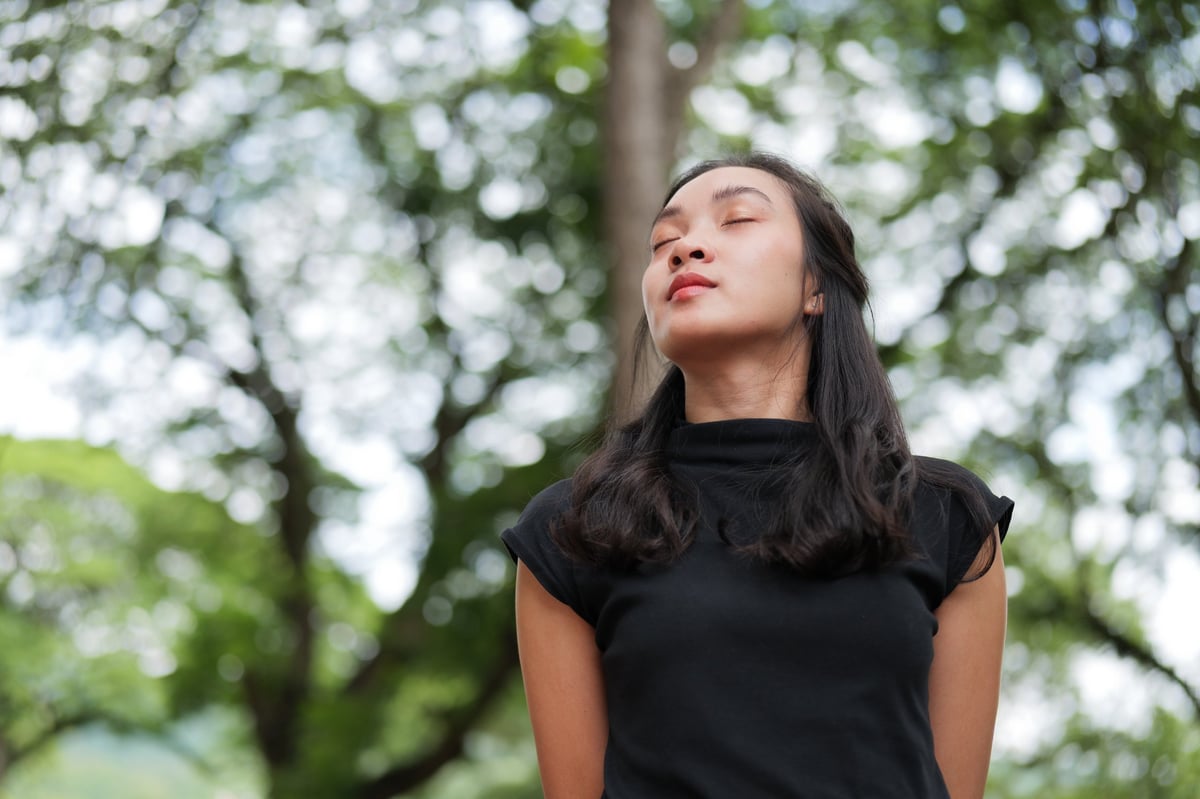 Young woman closing eyes, enjoying nature's calmness and fresh air