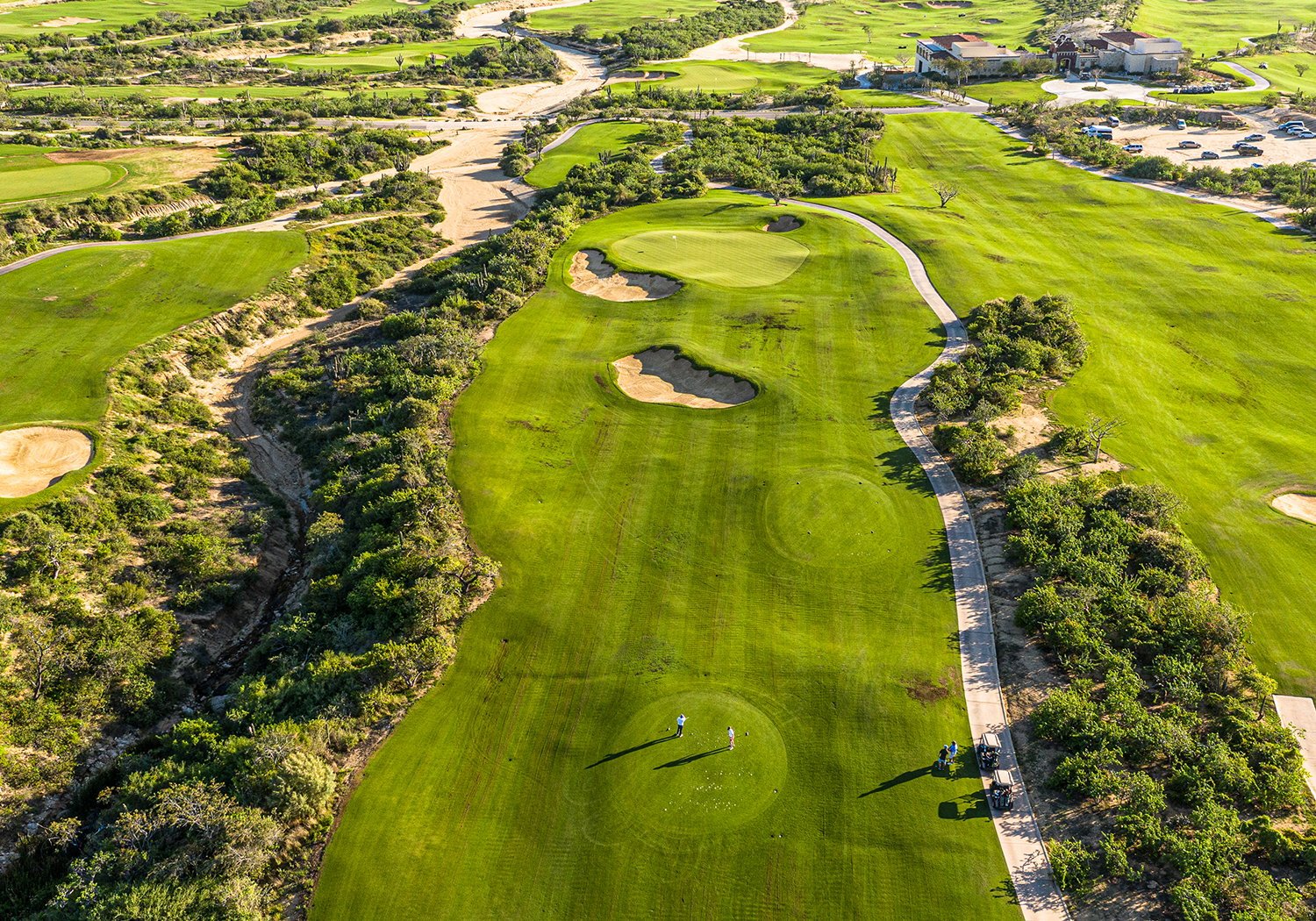 Aerial view of a manicured golf course with green fairways, sand bunkers, tree-lined borders, and a winding river