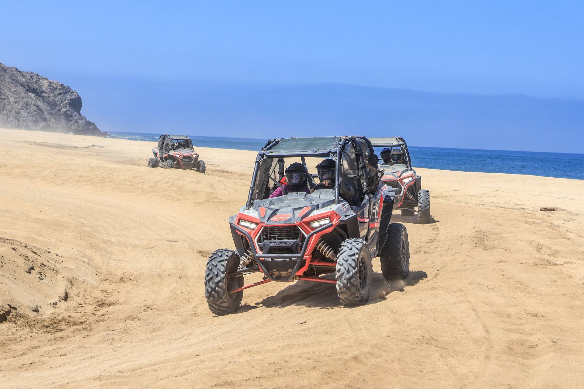 Red and white dune buggy on sandy beach with ocean and rocky cliffs in background