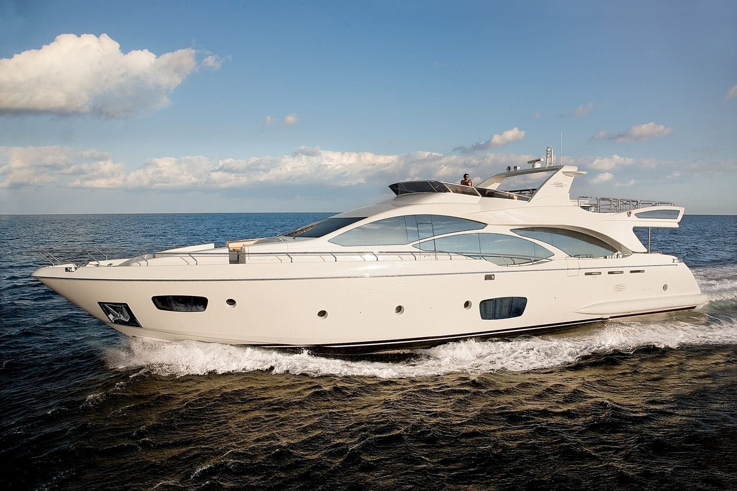 Luxurious white motor yacht anchored in shallow coastal water on a sunny day with blue sky and white clouds